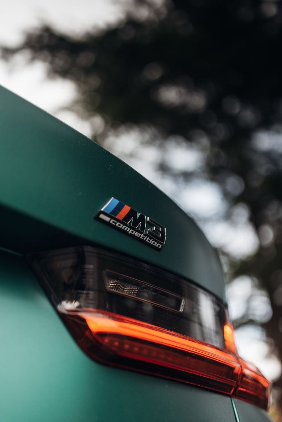 M3-Competition-Emblem und LED-Rückleuchte an einem BMW in Mattgrün